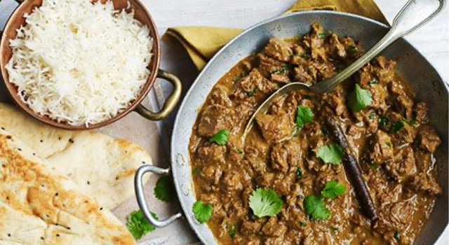 Slow cooked beef curry in a dish, with a bowl of rice on the side